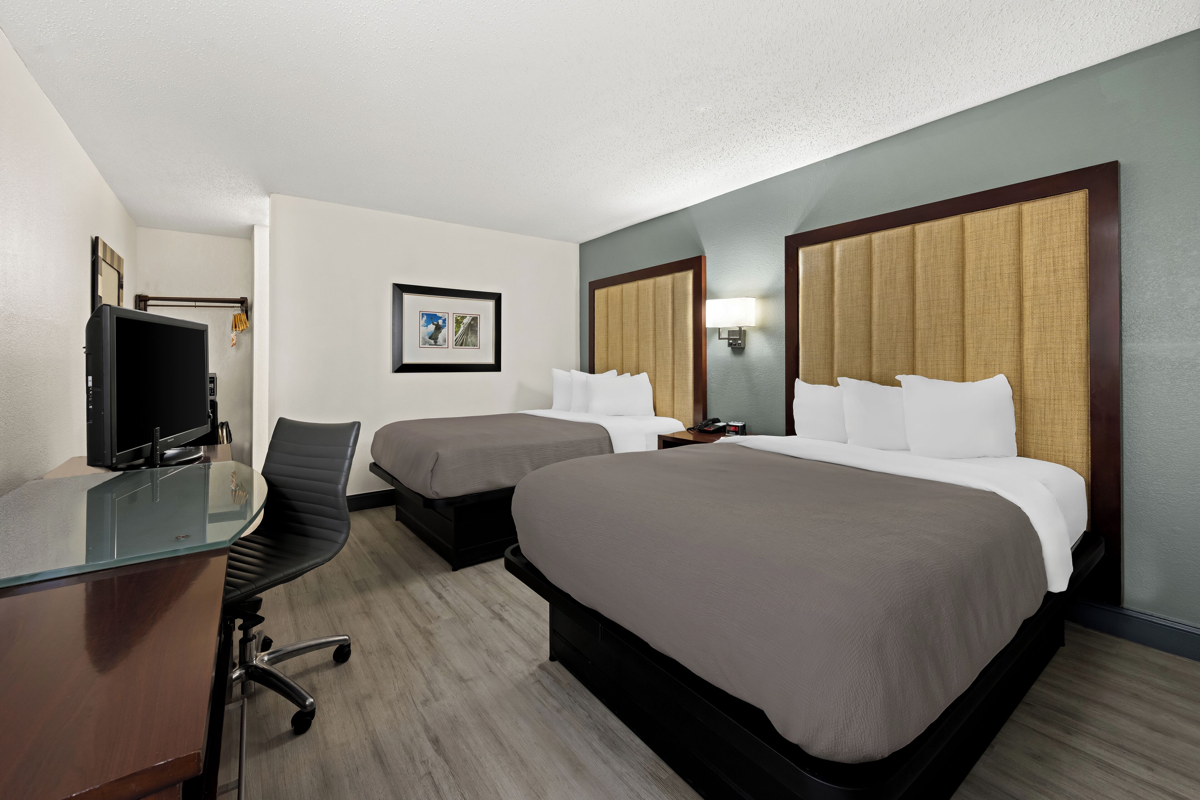 A hotel room with two beds, a desk with a computer, a chair, and a television.