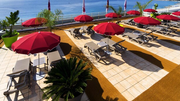 A rooftop terrace with sun loungers, red umbrellas, and potted plants. - Aparthotel Adagio Nice Promenade des Anglais (Nice)
