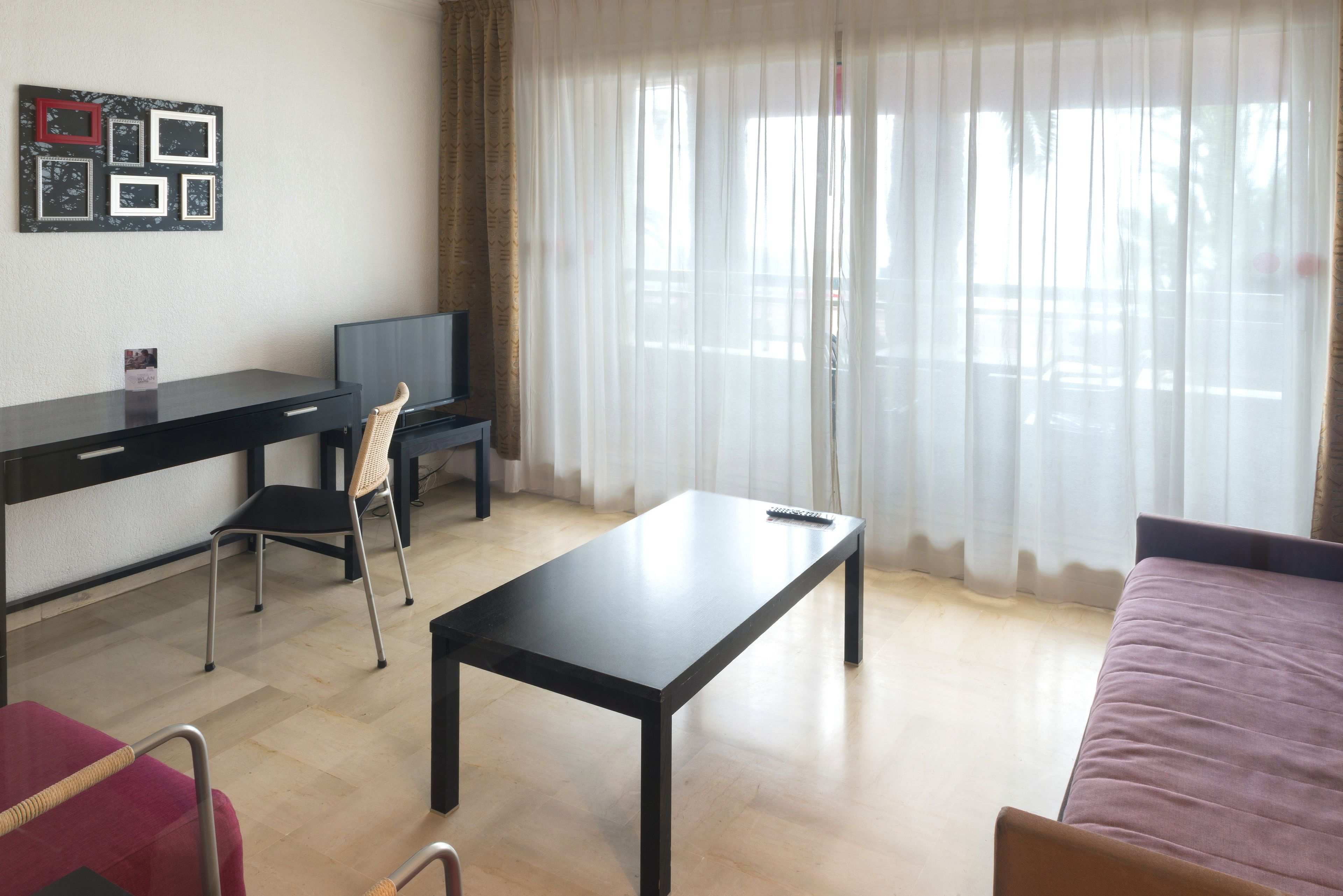 Una habitación con cama, un escritorio con silla, un televisor y una ventana con cortinas.