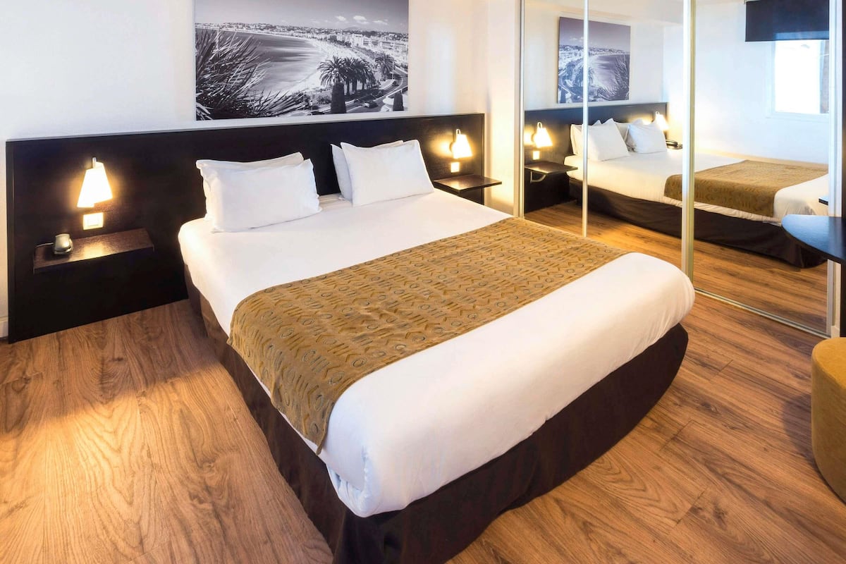 A hotel room with a large bed, bedside tables with lamps, a mirror, and a cityscape view.