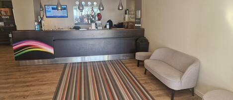 A modern reception area with a striped carpet, a grey sofa, and a reception desk with a digital screen.