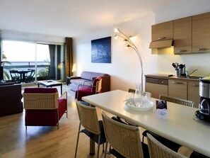 A modern hotel room with a balcony, a dining area, a sofa, and a kitchen. - Aparthotel Adagio Nice Promenade des Anglais (Nice)