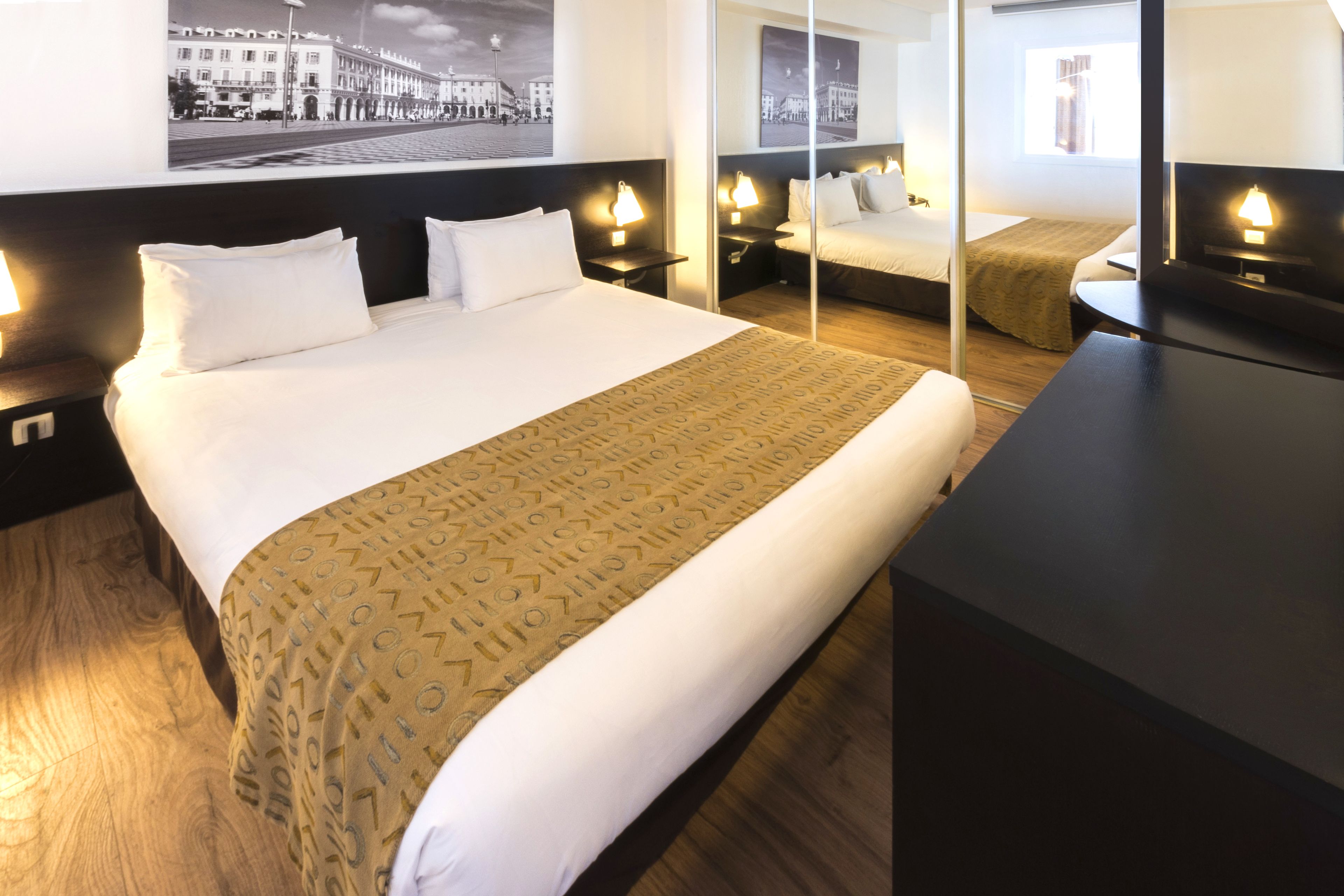 A hotel room with a large bed, bedside tables with lamps, a desk, and a mirror.