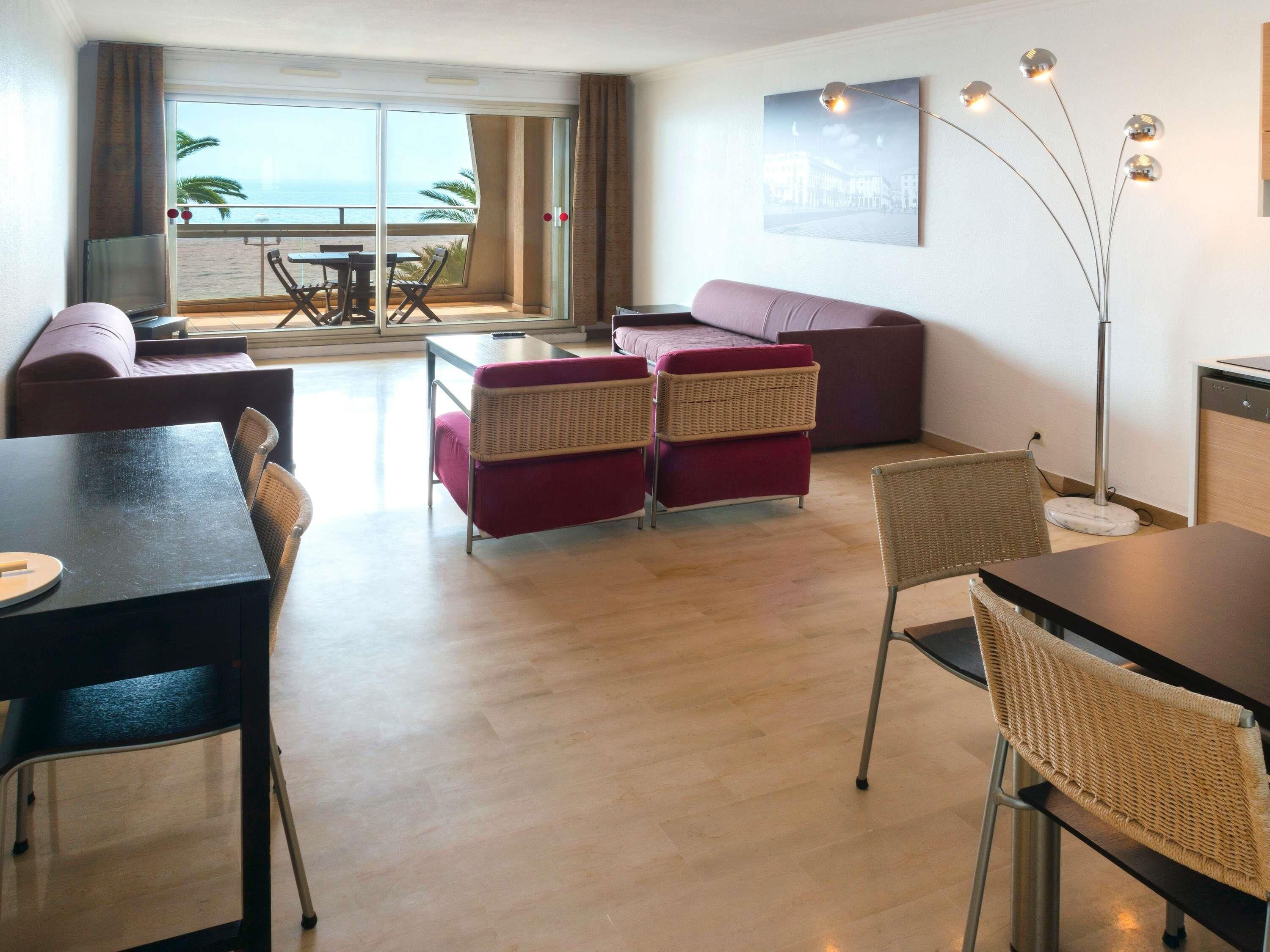 Un salon moderne comprenant un canapé, des fauteuils, une table à manger et offrant une vue sur la mer grâce à de grandes fenêtres.
