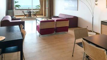 Een moderne woonkamer met een bank, stoelen, een eettafel en uitzicht op zee door grote ramen.
