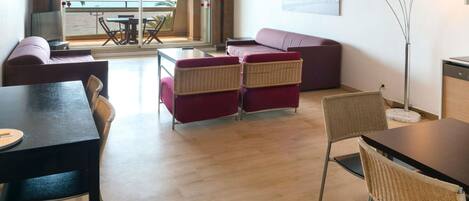 Un salon moderne comprenant un canapé, des fauteuils, une table à manger et offrant une vue sur la mer grâce à de grandes fenêtres.