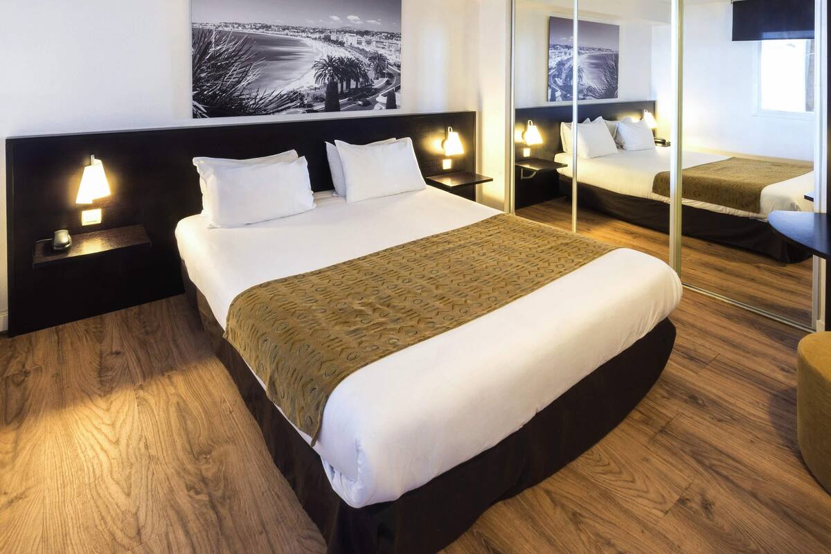 A hotel room with a large bed, two bedside tables with lamps, a large mirror, and a cityscape view.