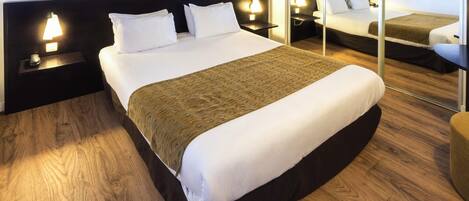 A hotel room with a large bed, two bedside tables with lamps, a large mirror, and a cityscape view.