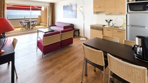 A modern kitchen with a microwave, refrigerator, and dining area with wicker chairs and a table. - Aparthotel Adagio Nice Promenade des Anglais (Nice)