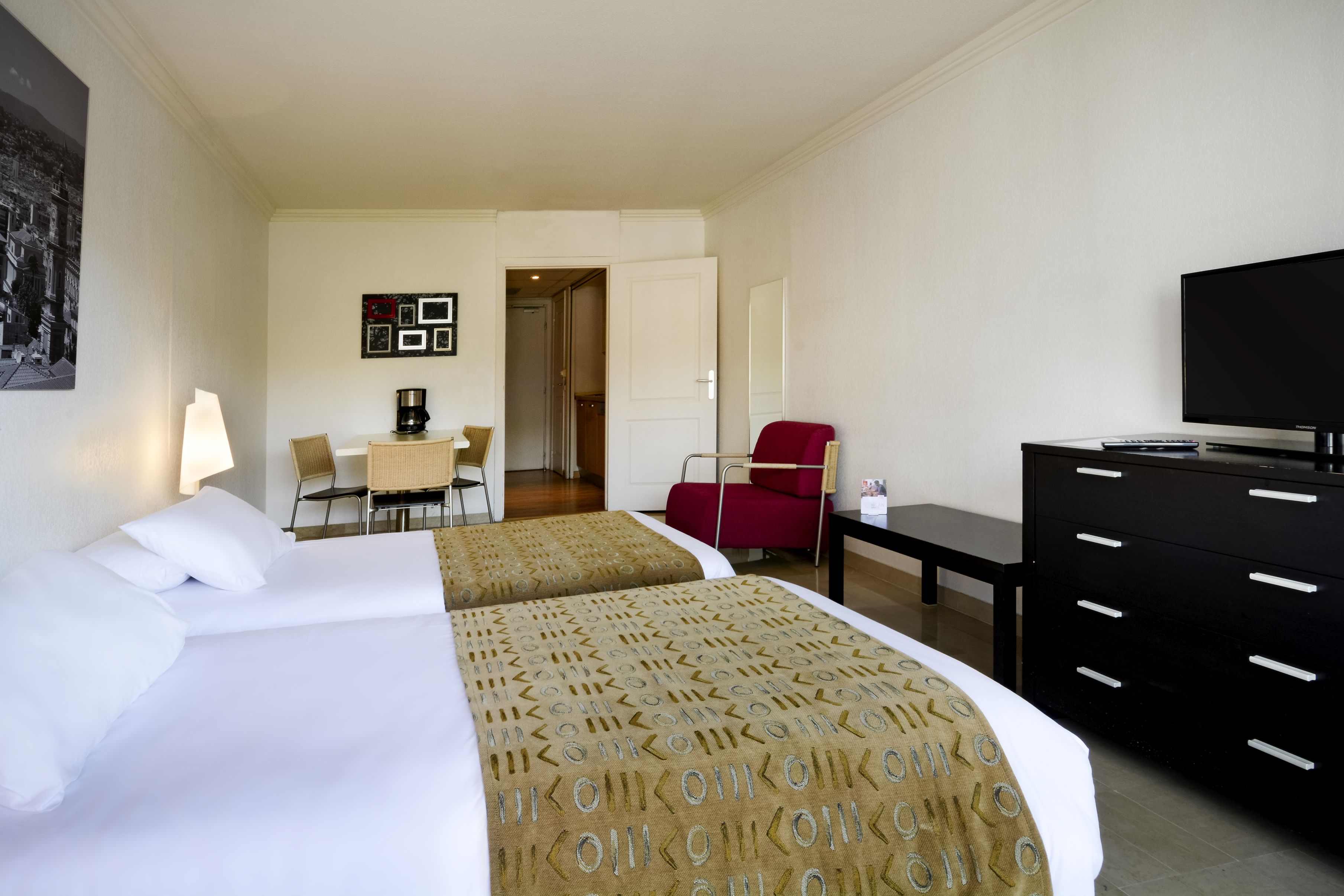 Une chambre d’hôtel avec deux lits, un bureau, une chaise, une télévision et une commode.
