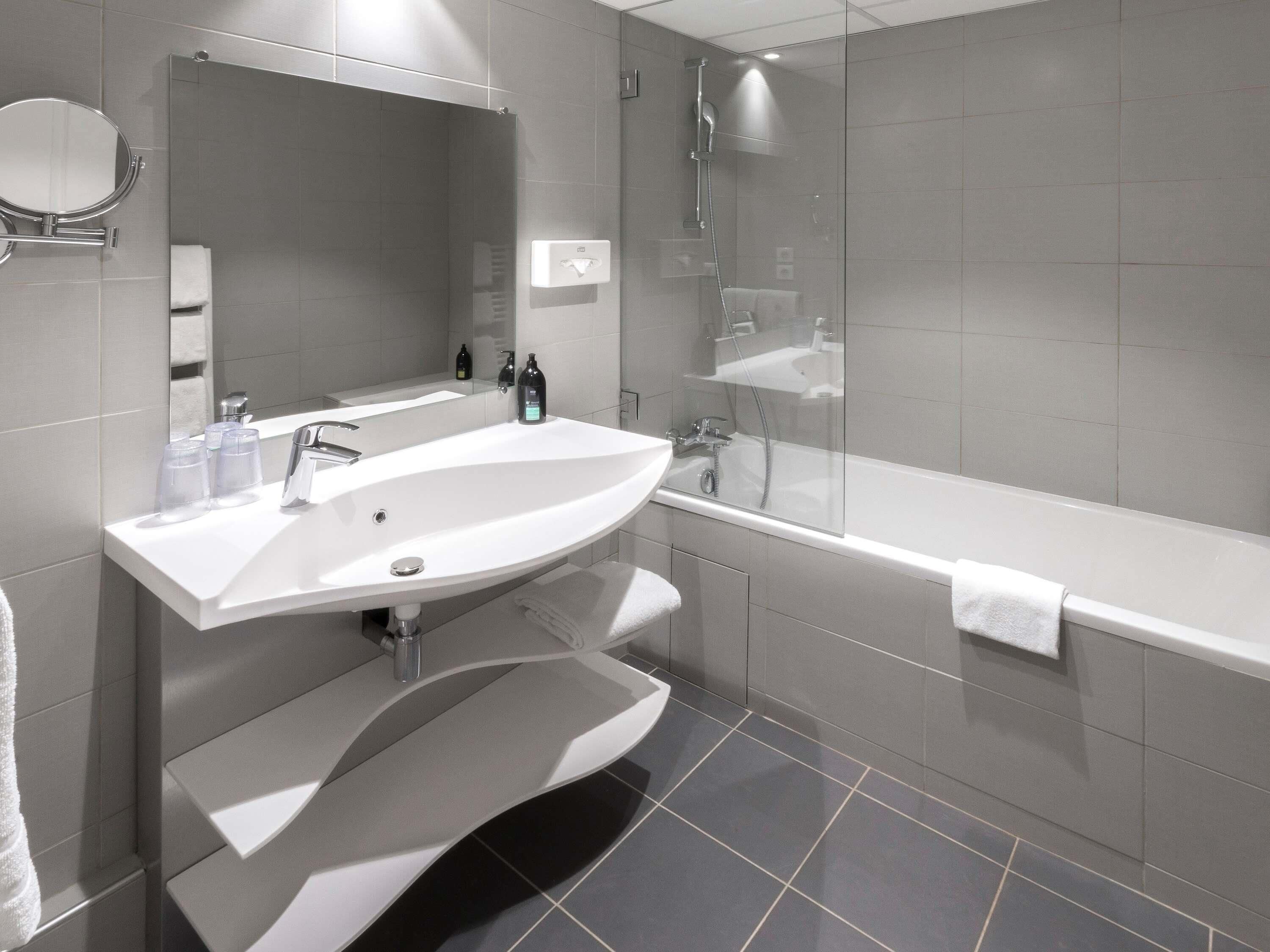 Une salle de bain moderne avec un grand lavabo blanc, un miroir, une douche à l’italienne et une baignoire blanche.