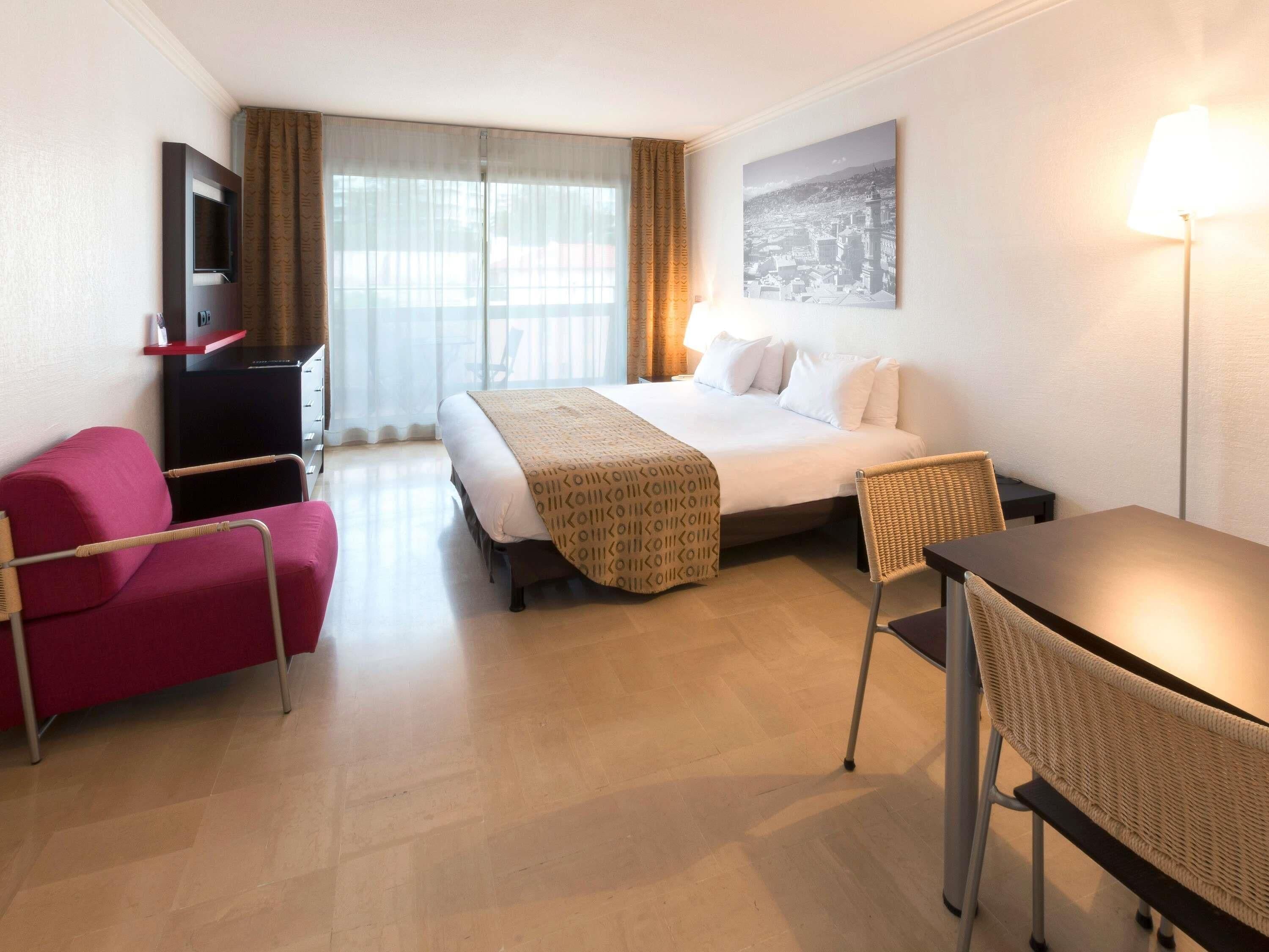 A hotel room with a bed, a desk, a chair, a television, and a window with curtains.