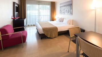 Une chambre d’hôtel avec un lit, un bureau, une chaise, une télévision et une fenêtre avec des rideaux.