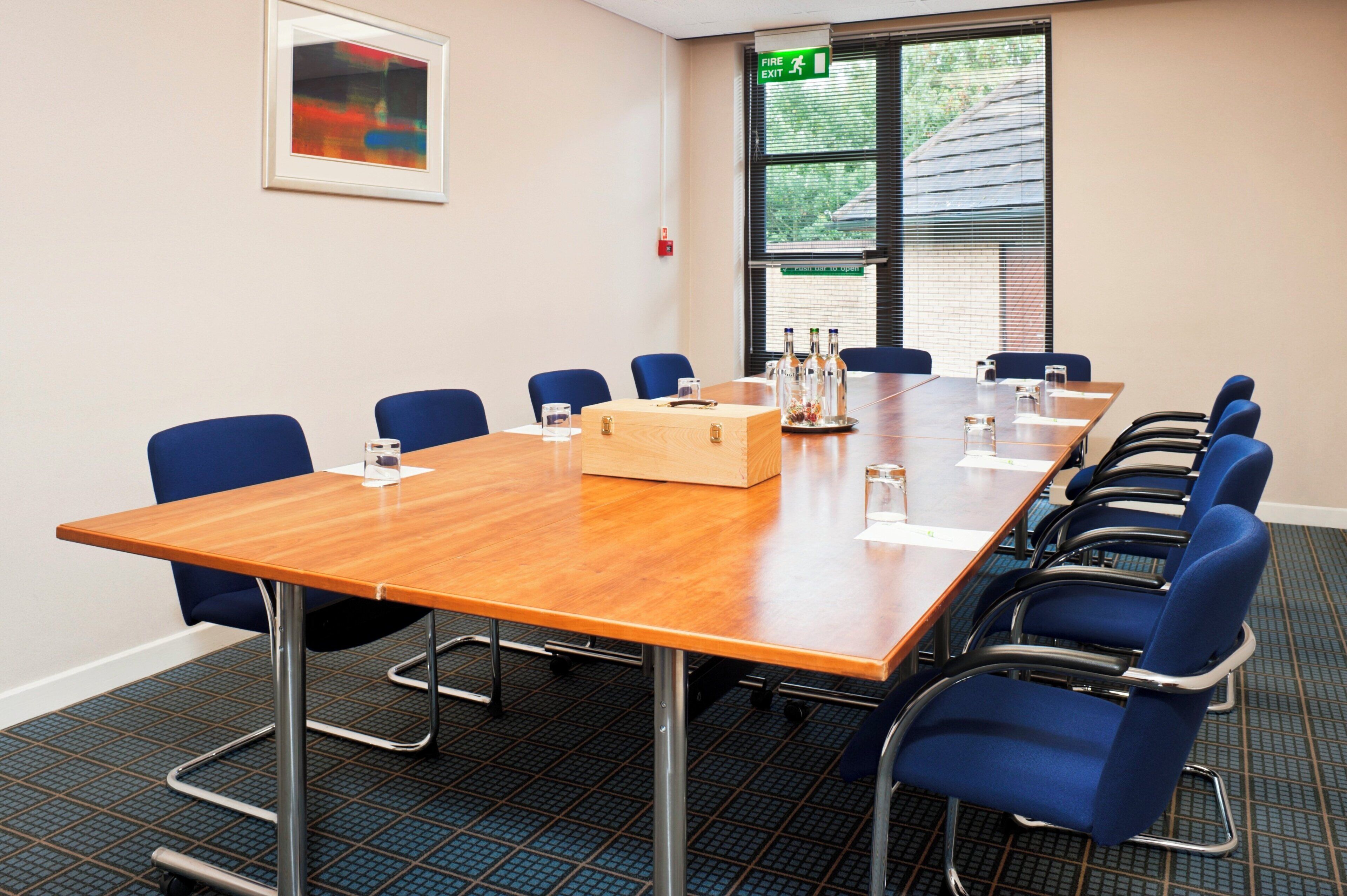 A conference room with a long table, blue chairs, a wooden box, and a fire exit sign.