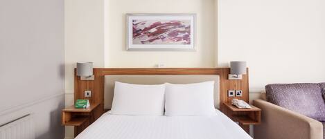 A hotel room with a large bed, two bedside tables with lamps, a chair, a painting on the wall, and a phone on the nightstand.