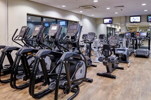 Un gimnasio con varias máquinas de cardio, incluyendo cintas de correr y elípticas, dispuestas en filas.