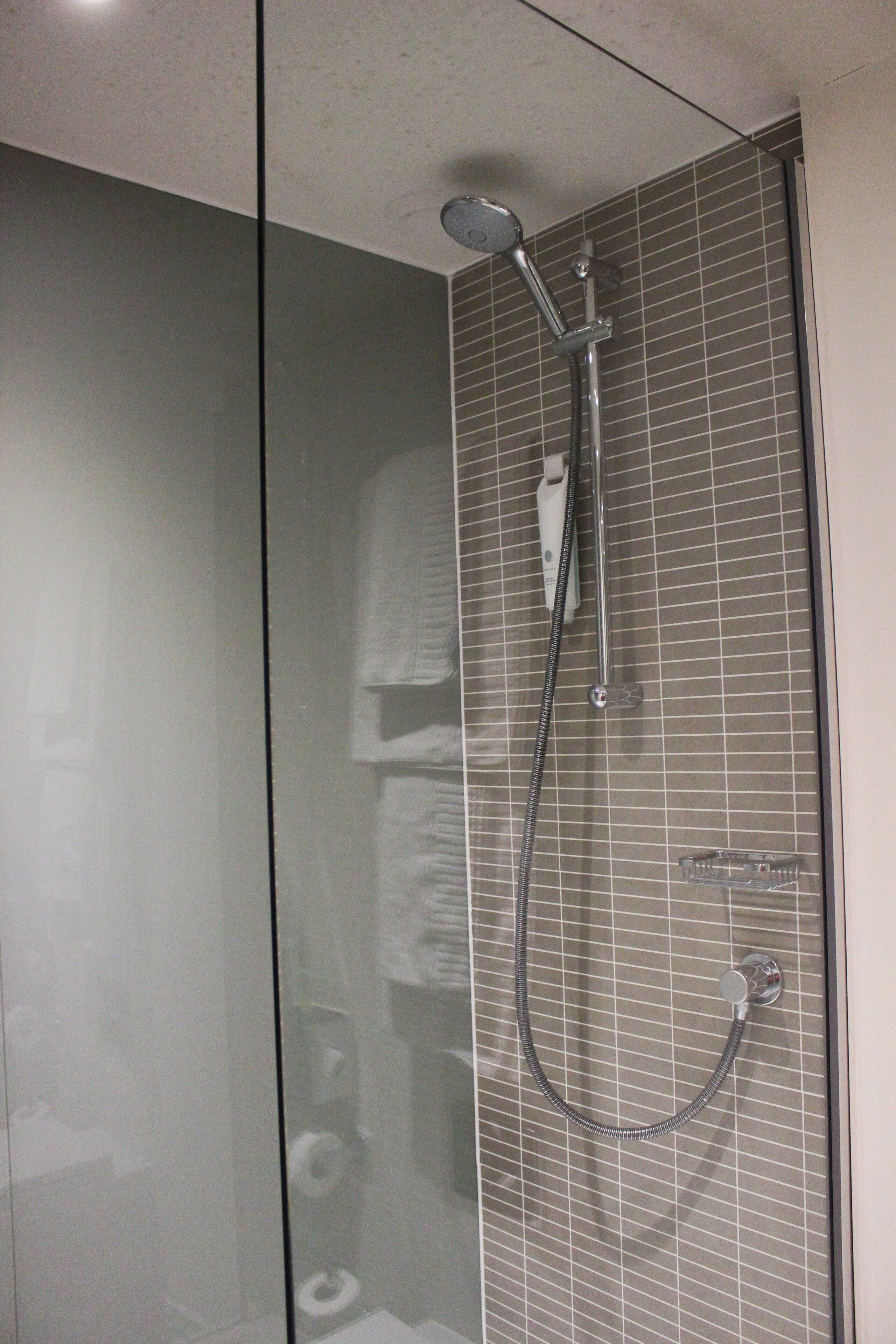 Une douche fermée par des parois en verre, dotée d’un pommeau de douche à main et d’un robinet mural.