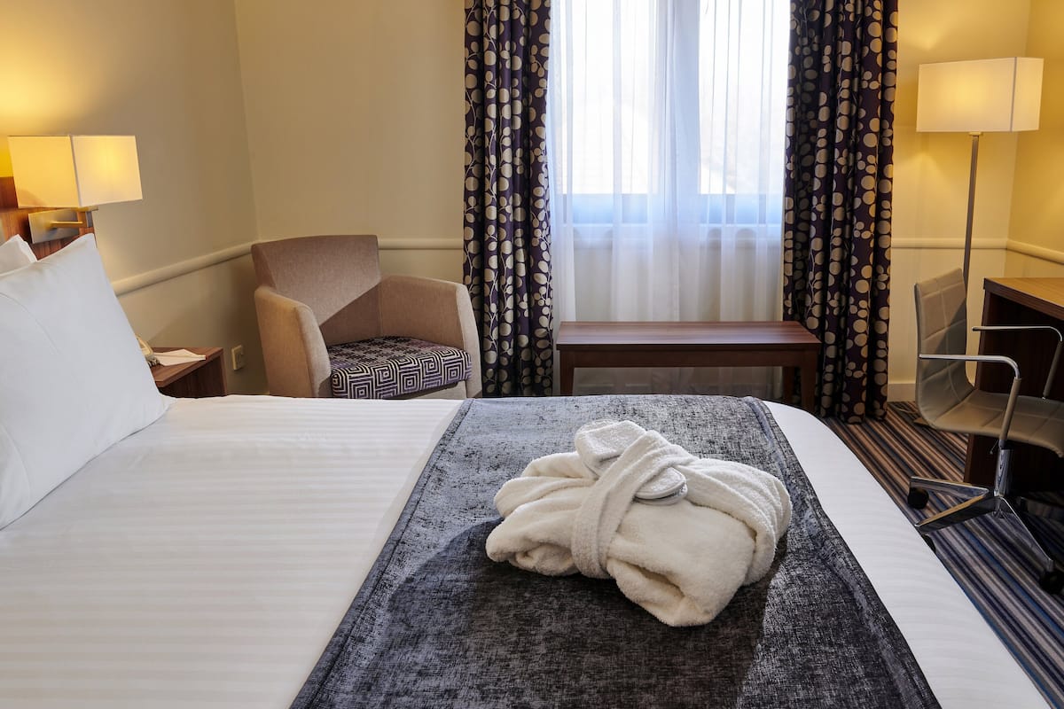Ein Hotelzimmer mit Bett, Sessel, Schreibtisch und Fernseher.