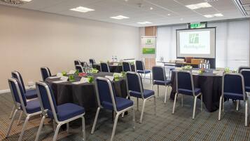 A conference room with tables, chairs, a projector screen displaying a Holiday Inn logo, and a welcome sign.