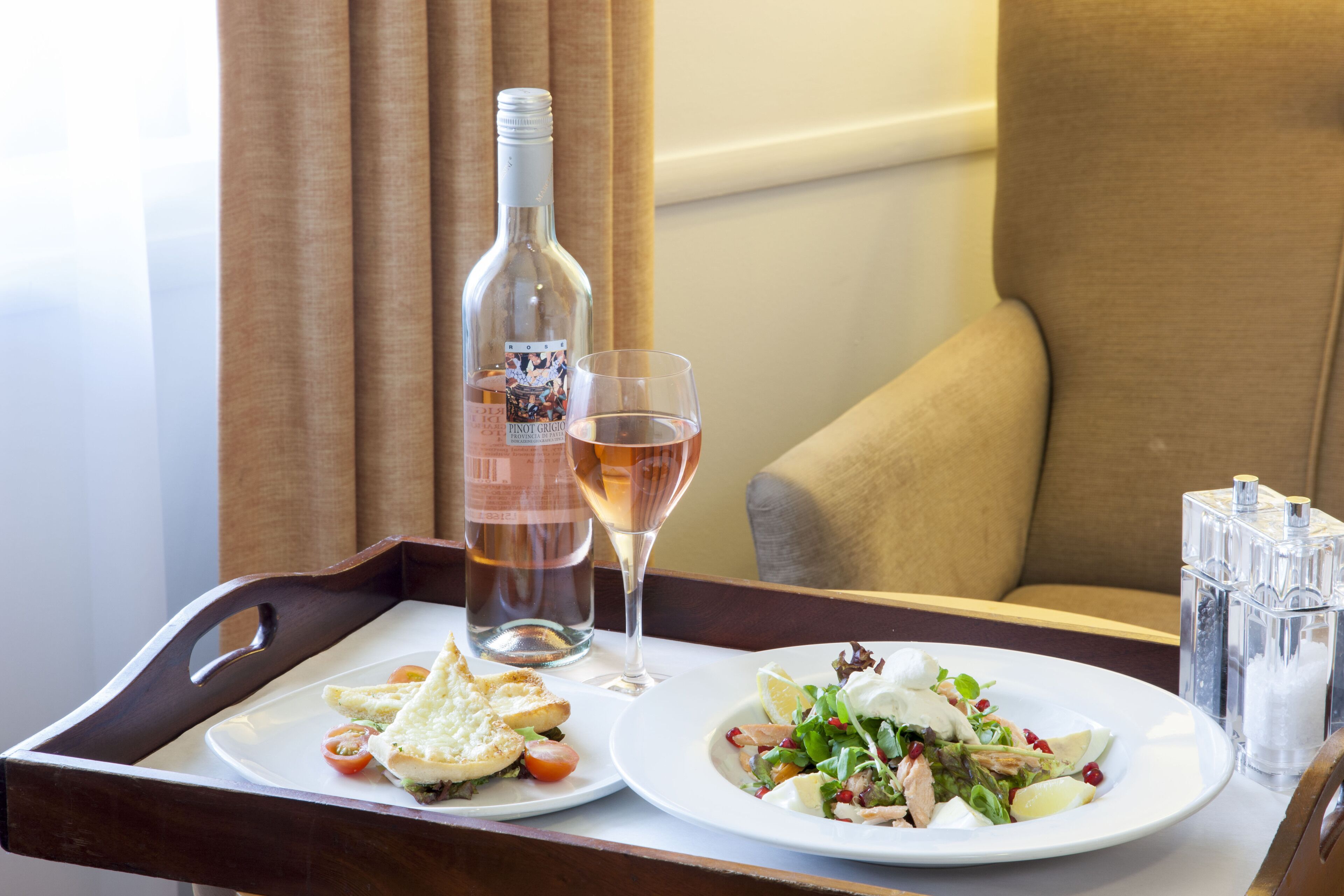 A tray with a bottle of wine, a glass of wine, and two plates of food on a table in a room.