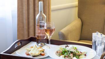 A tray with a bottle of wine, a glass of wine, and two plates of food on a table in a room.