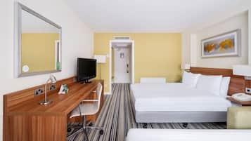 A hotel room with a bed, a desk with a computer, a chair, a TV, a mirror, a painting, and a telephone.