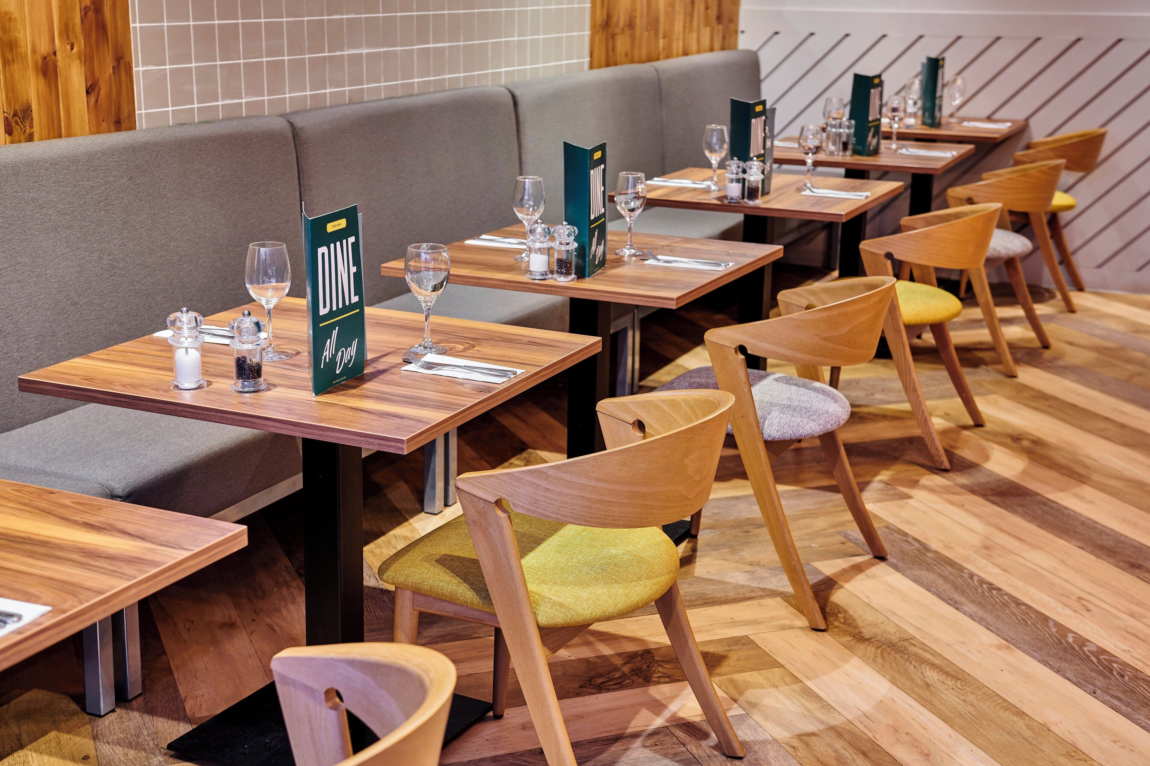 Un interior de restaurante con mesas de madera, asientos acolchados y un atril para el menú.