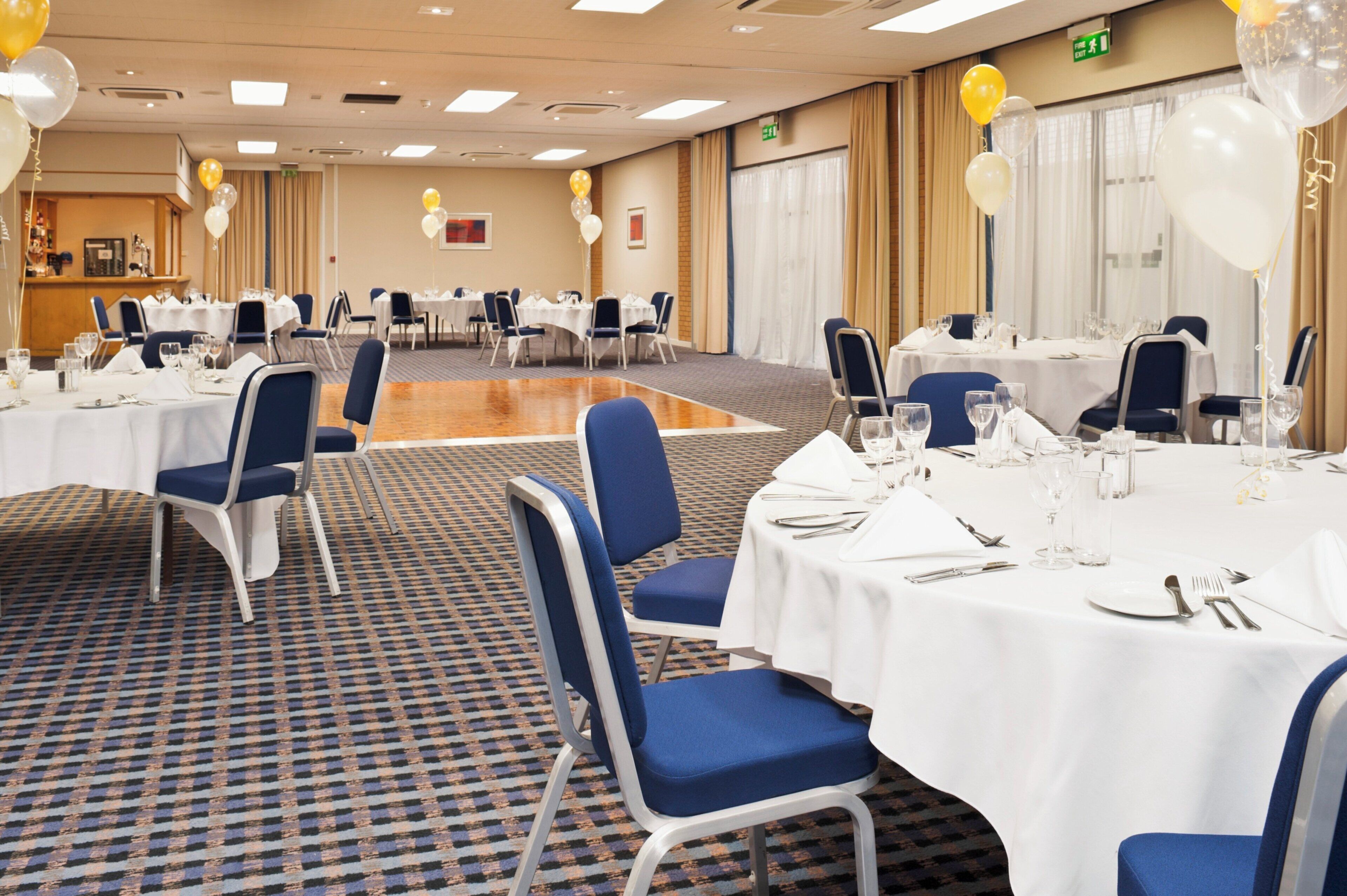 A banquet hall with round tables, chairs, and a carpeted floor.