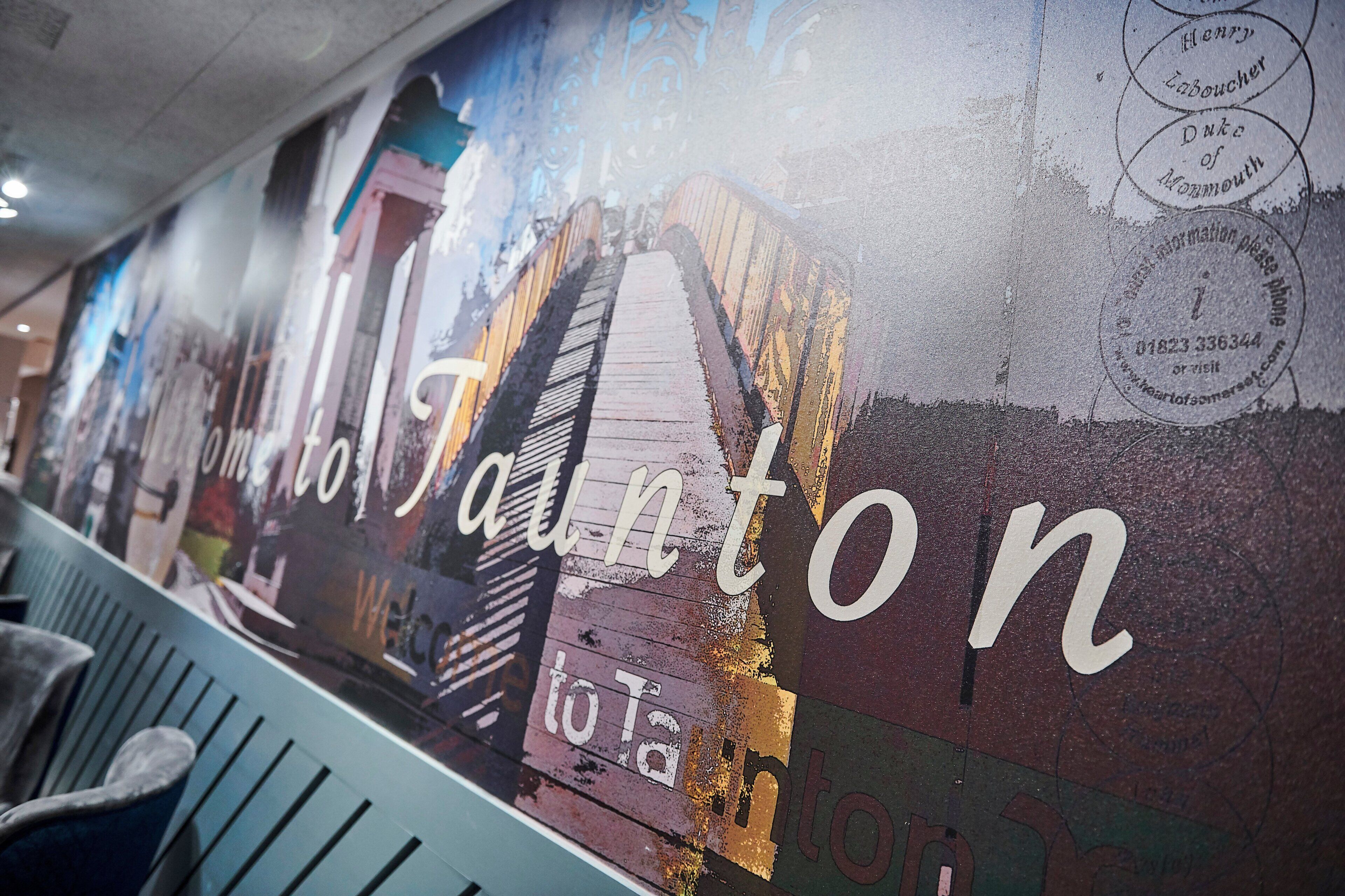 A wall with a mural of a building and the text 'Welcome to Hampton'.