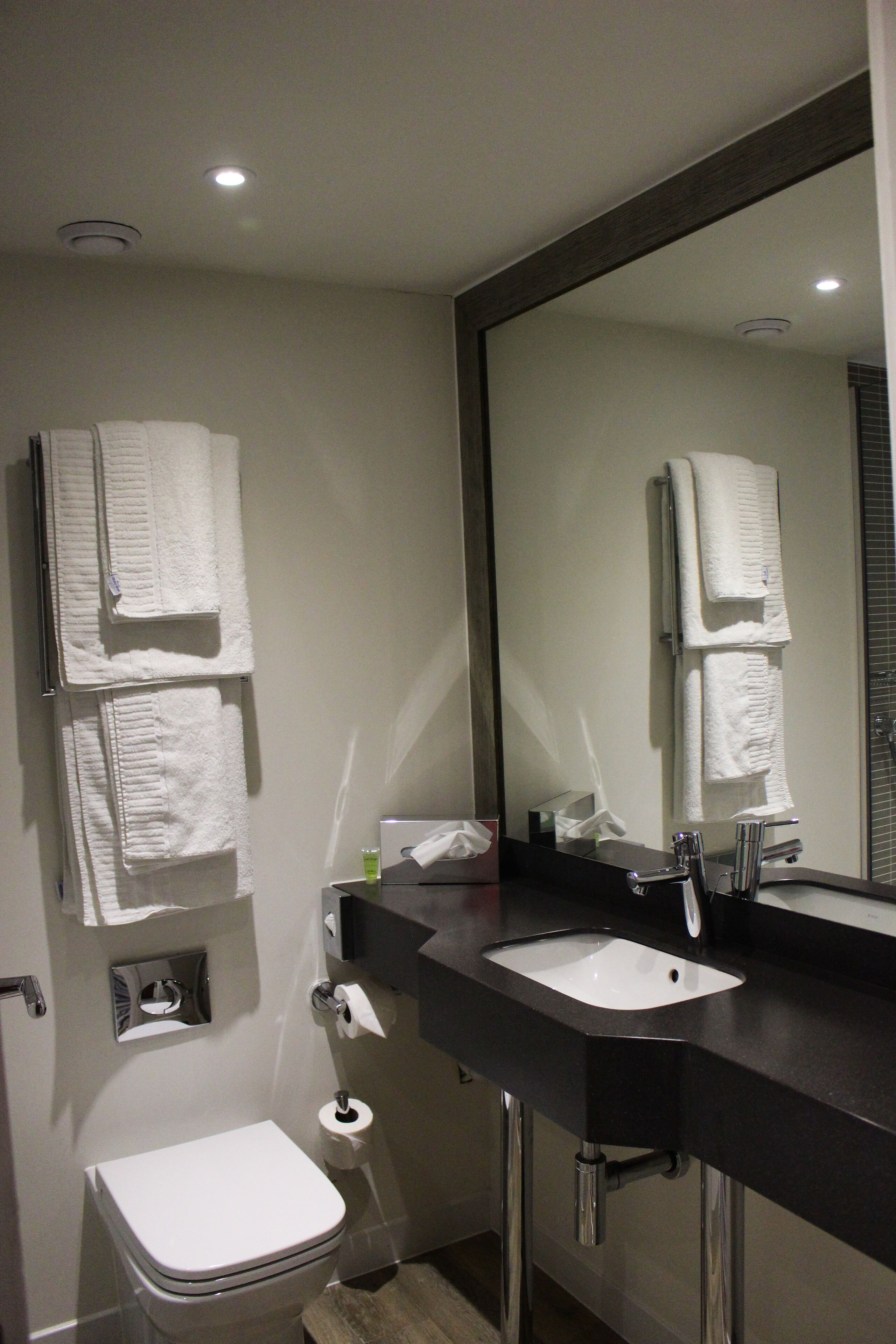 Un baño moderno con inodoro blanco, lavamanos negro y un espejo grande.