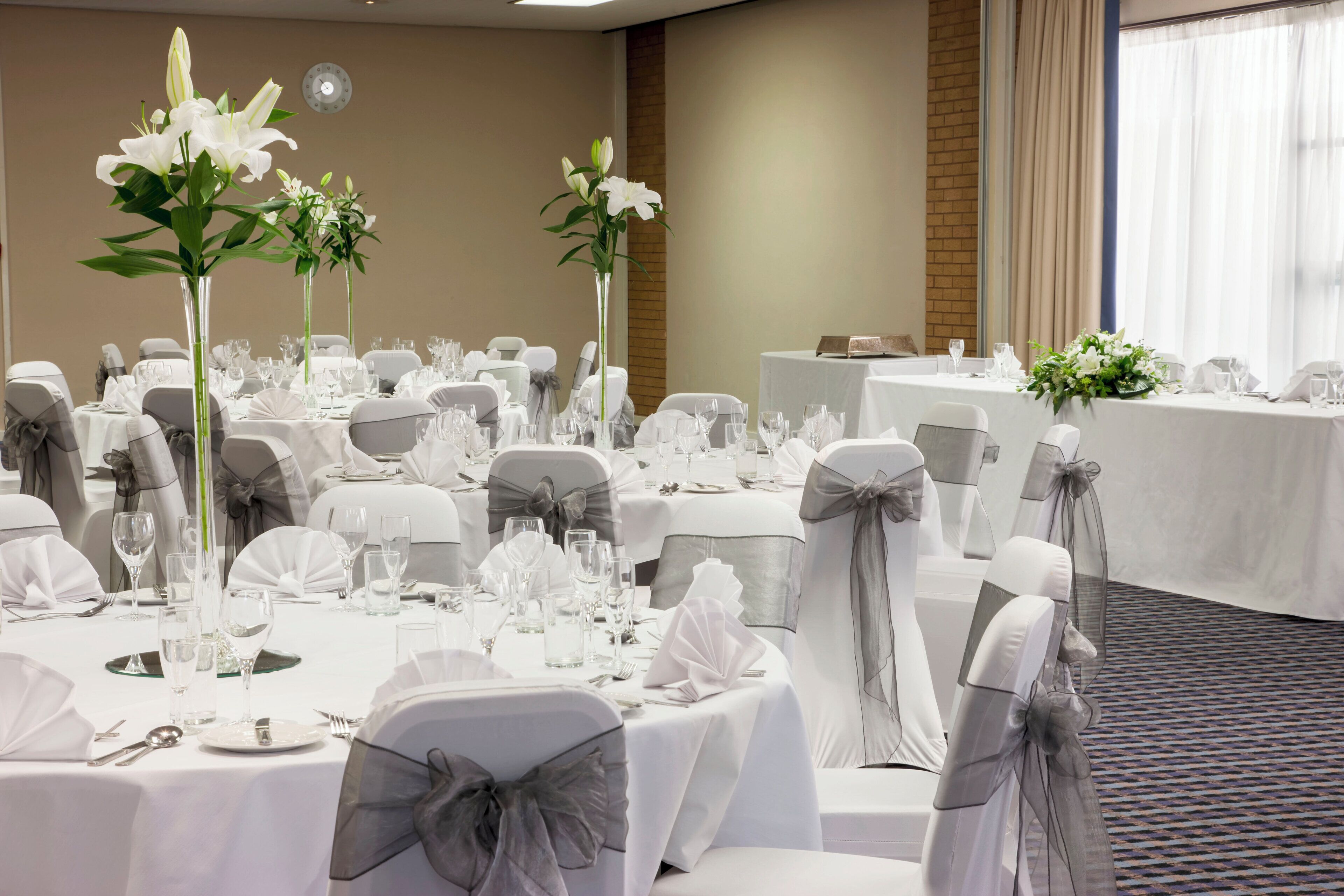 A banquet hall with round tables set for dining, each with white tablecloths, silverware, and clear glassware.