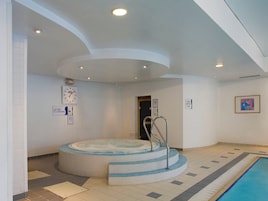 Una amplia piscina cubierta con un jacuzzi, suelo de baldosas y un reloj en la pared.