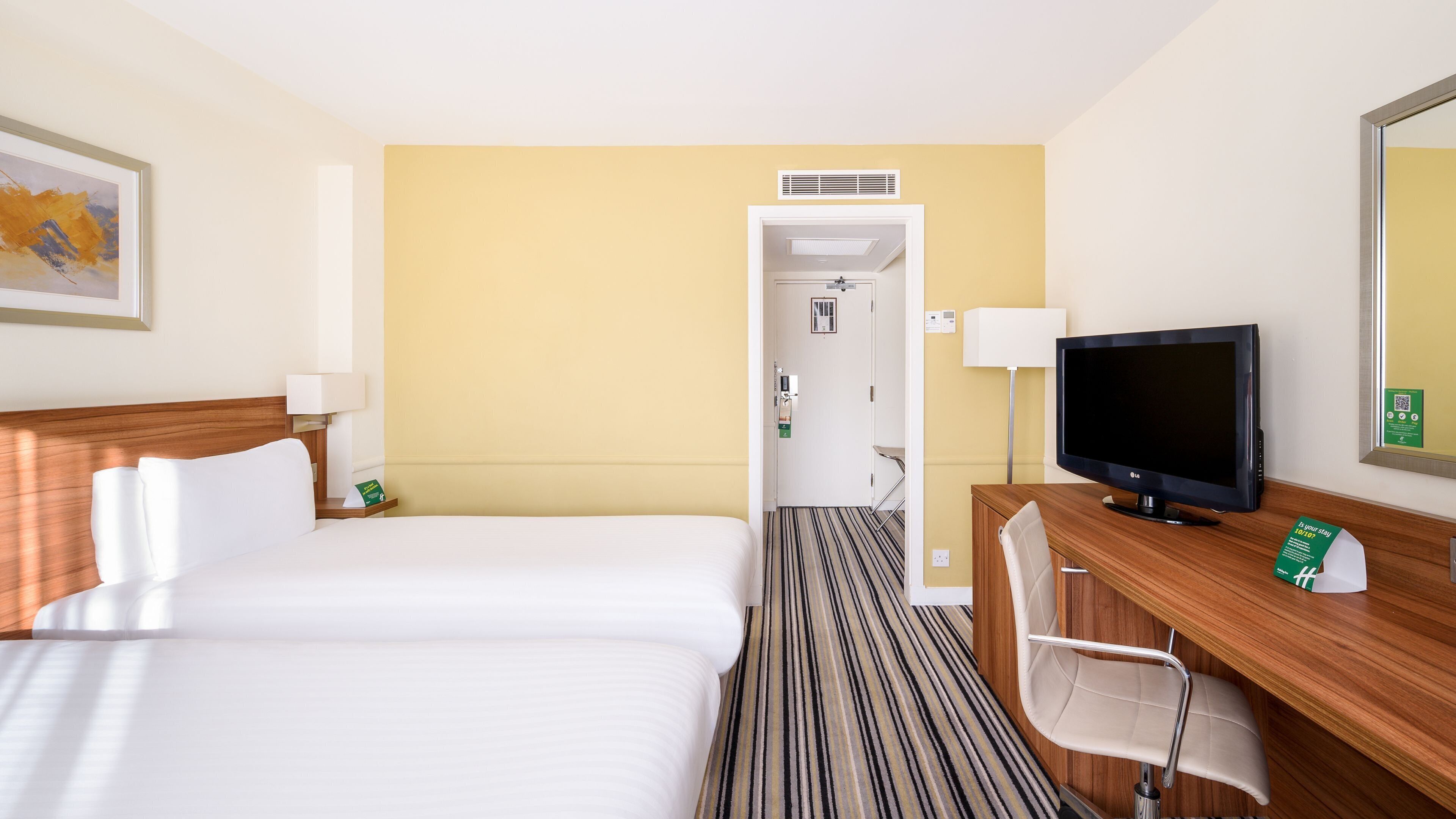 Ett hotellrum med två sängar, ett skrivbord med en tv, en stol och en dörr som leder till ett badrum.