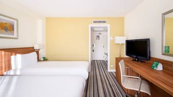 A hotel room with two beds, a desk with a TV, a chair, and a door leading to a bathroom.