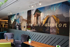 L’intérieur d’un restaurant, avec une fresque murale, des tables et un panneau indiquant : « Bienvenue à Salton. »