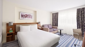 Une chambre d’hôtel avec un grand lit, un canapé, un fauteuil, une petite table et un tableau au mur.