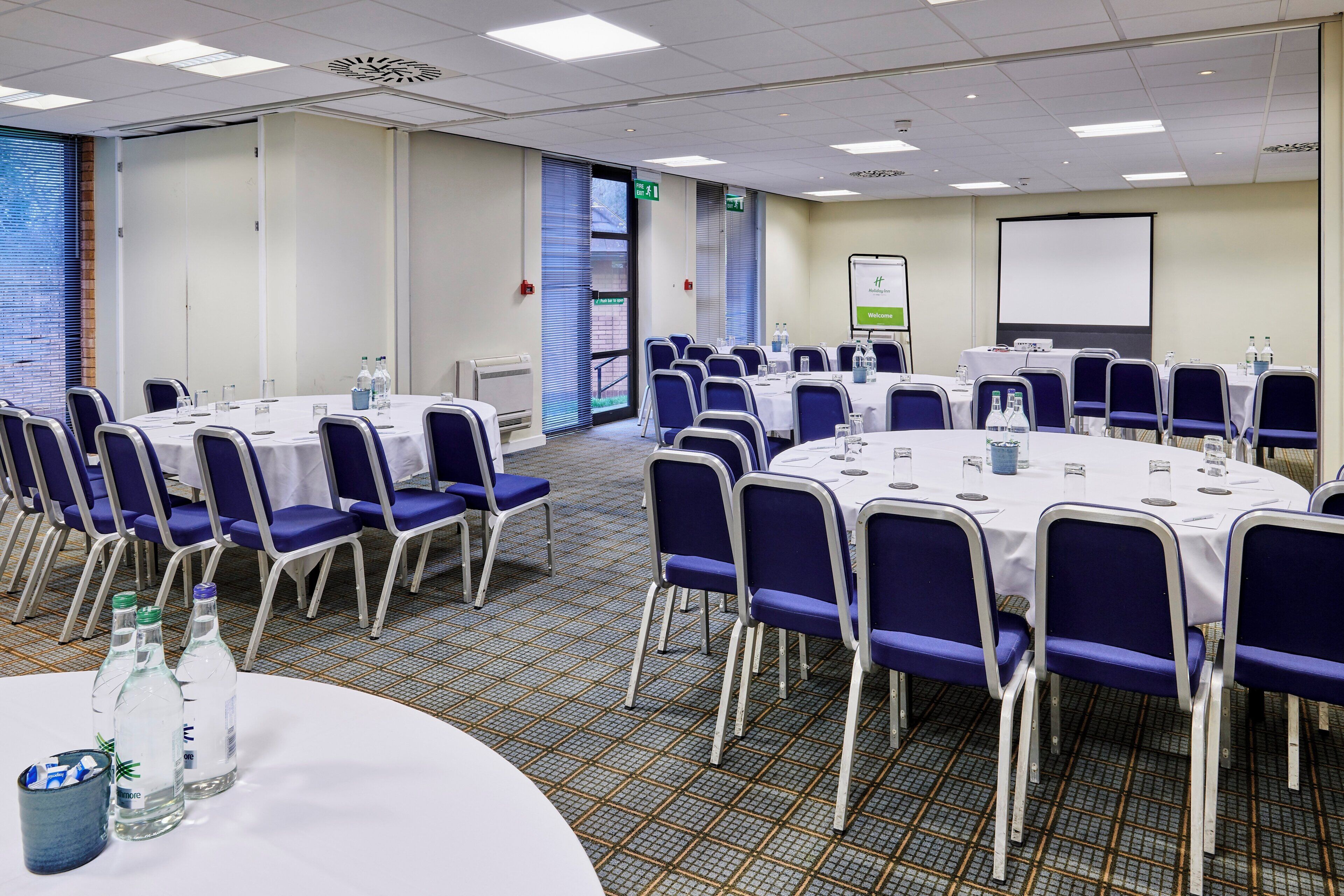 A conference room with round tables, chairs, and a projector screen.