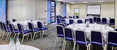 A conference room with round tables, chairs, and a projector screen.