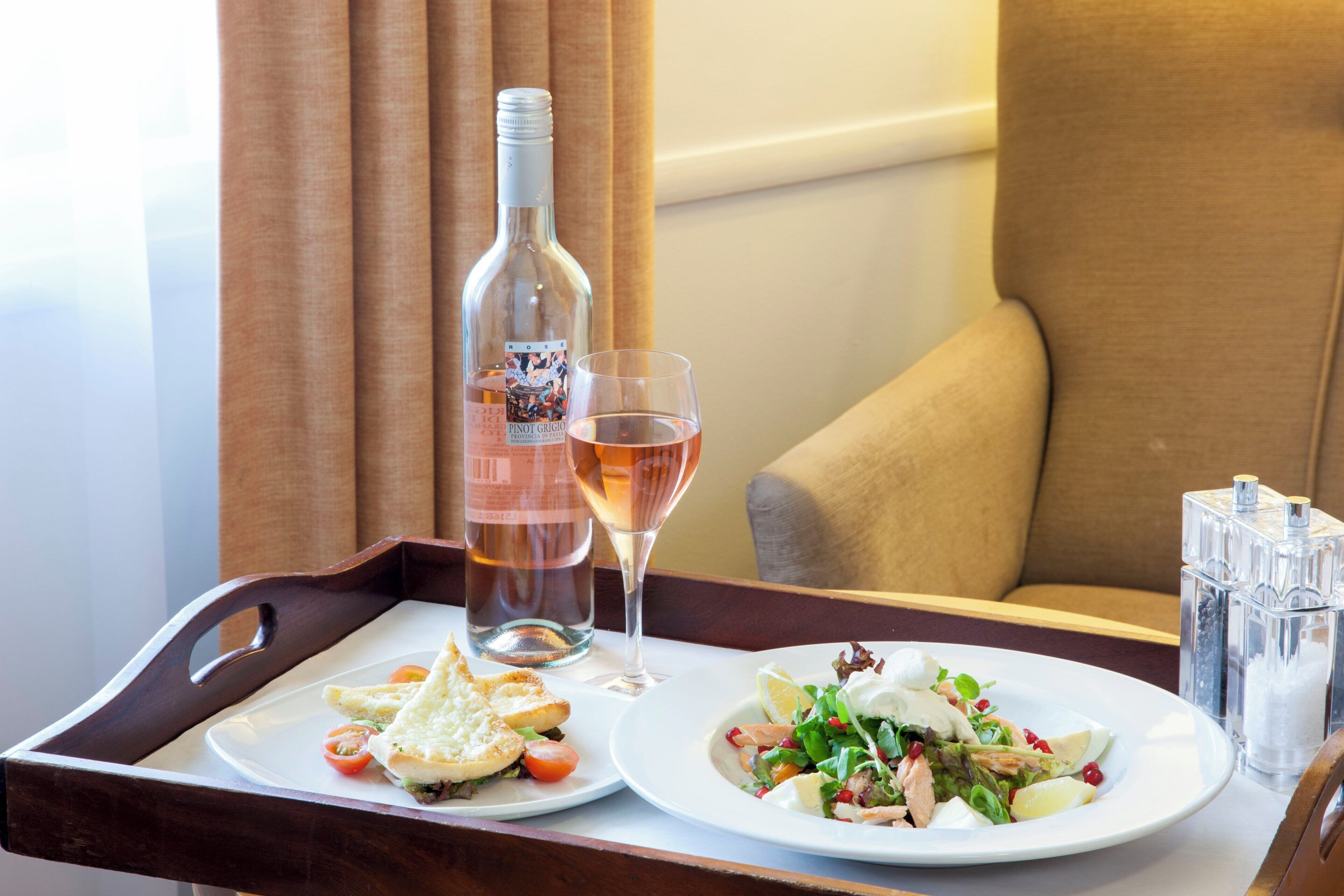 A tray with a bottle of wine, a glass of wine, a plate with a sandwich, and a salad.