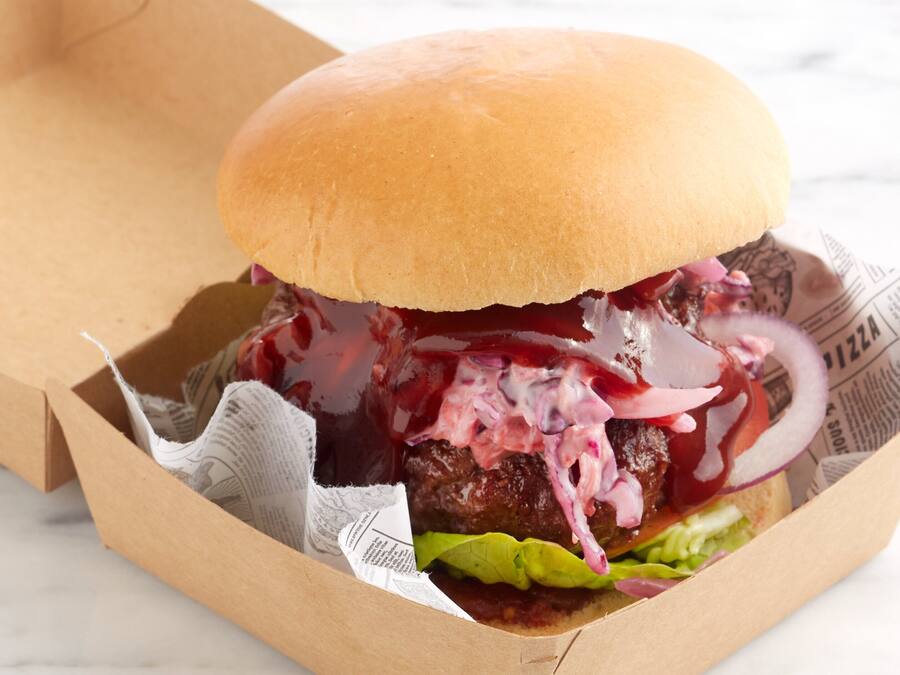 A burger in a paper container with a bun, lettuce, and red onion.