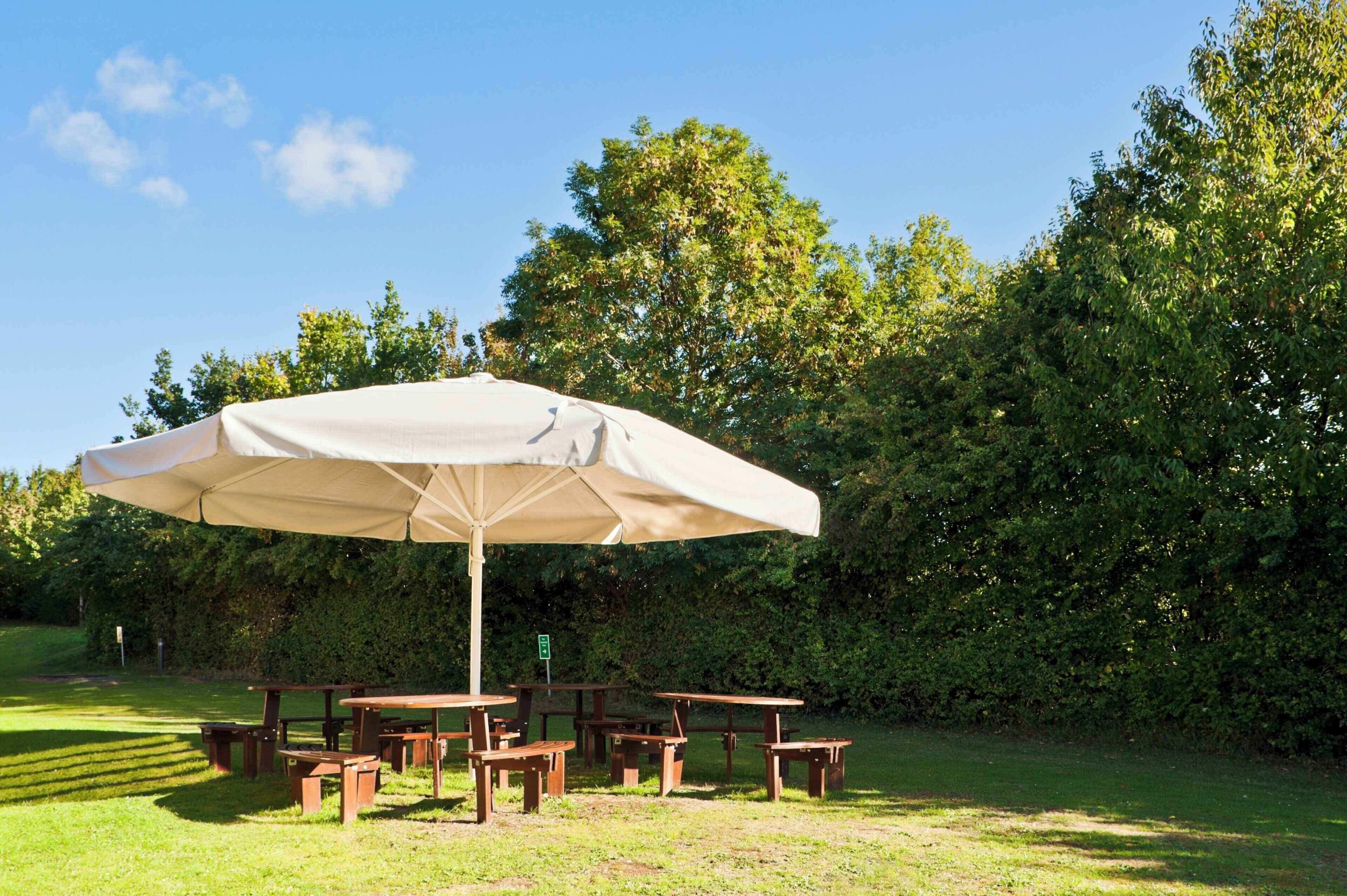 A picnic area with a large umbrella, wooden benches, and picnic tables.