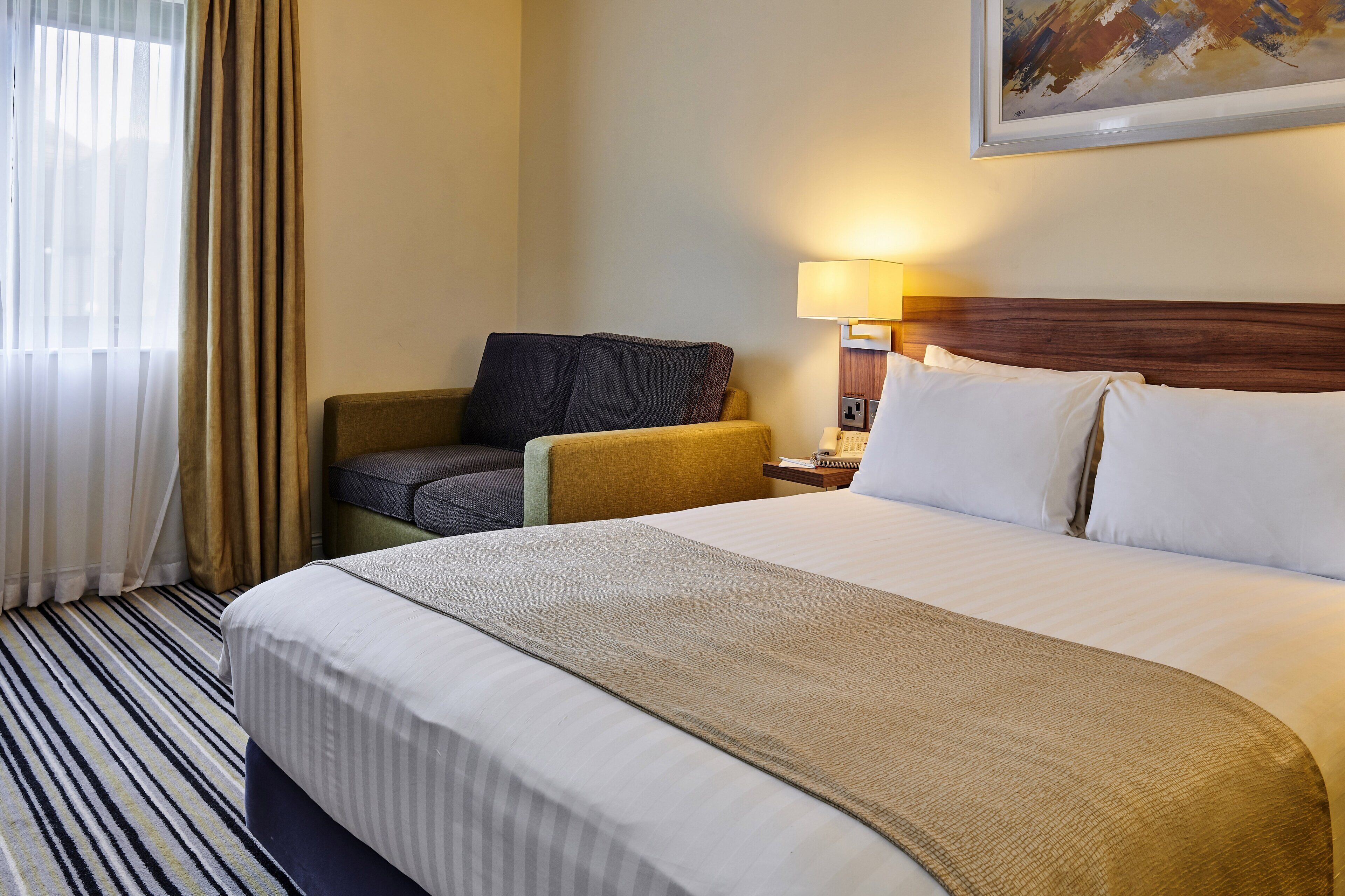 Une chambre d’hôtel avec un lit, une chaise, une lampe et un tableau au mur.