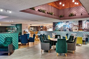 Un café moderno con diversas opciones de asiento, incluidas sillas y mesas, y una zona de bar con un mural de la ciudad.