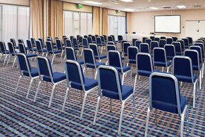 A conference room with rows of blue chairs, a projector screen, and an exit sign. - Holiday Inn Taunton by IHG (Taunton)
