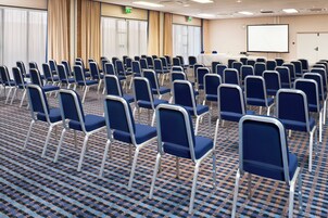 Un salón de conferencias con filas de sillas azules, una pantalla de proyector y una señal de salida.
