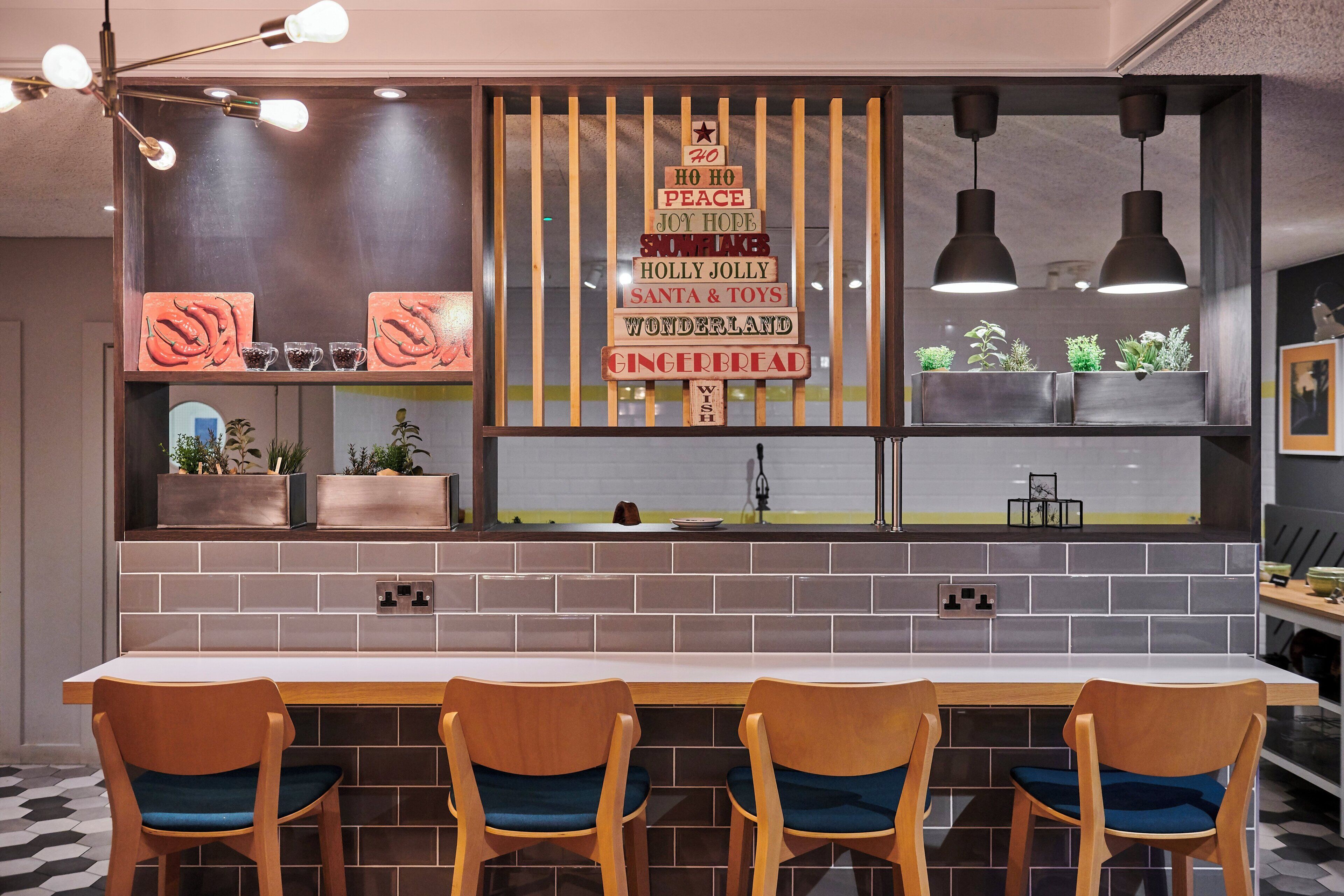 A modern kitchen with a long counter, wooden chairs, and a decorative sign with holiday greetings.