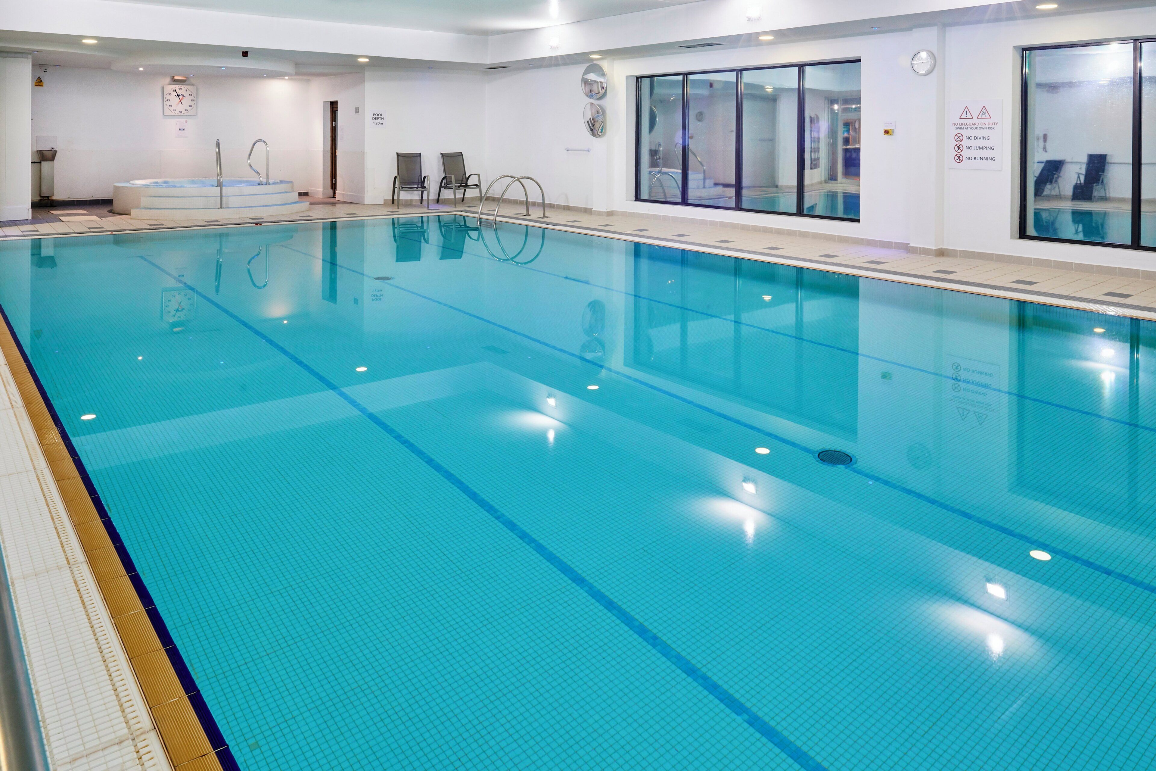 A large indoor swimming pool with clear water, marked lanes, and safety signs on the walls.
