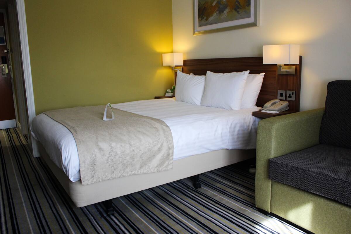 A hotel room with a bed, bedside lamps, a telephone, and a chair.