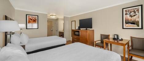 A hotel room with a large bed, a desk, a chair, a television, and artwork on the walls.