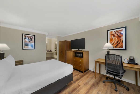 Ein Hotelzimmer mit einem Bett, einem Schreibtisch mit Computer, einem Fernseher und einer Mikrowelle.